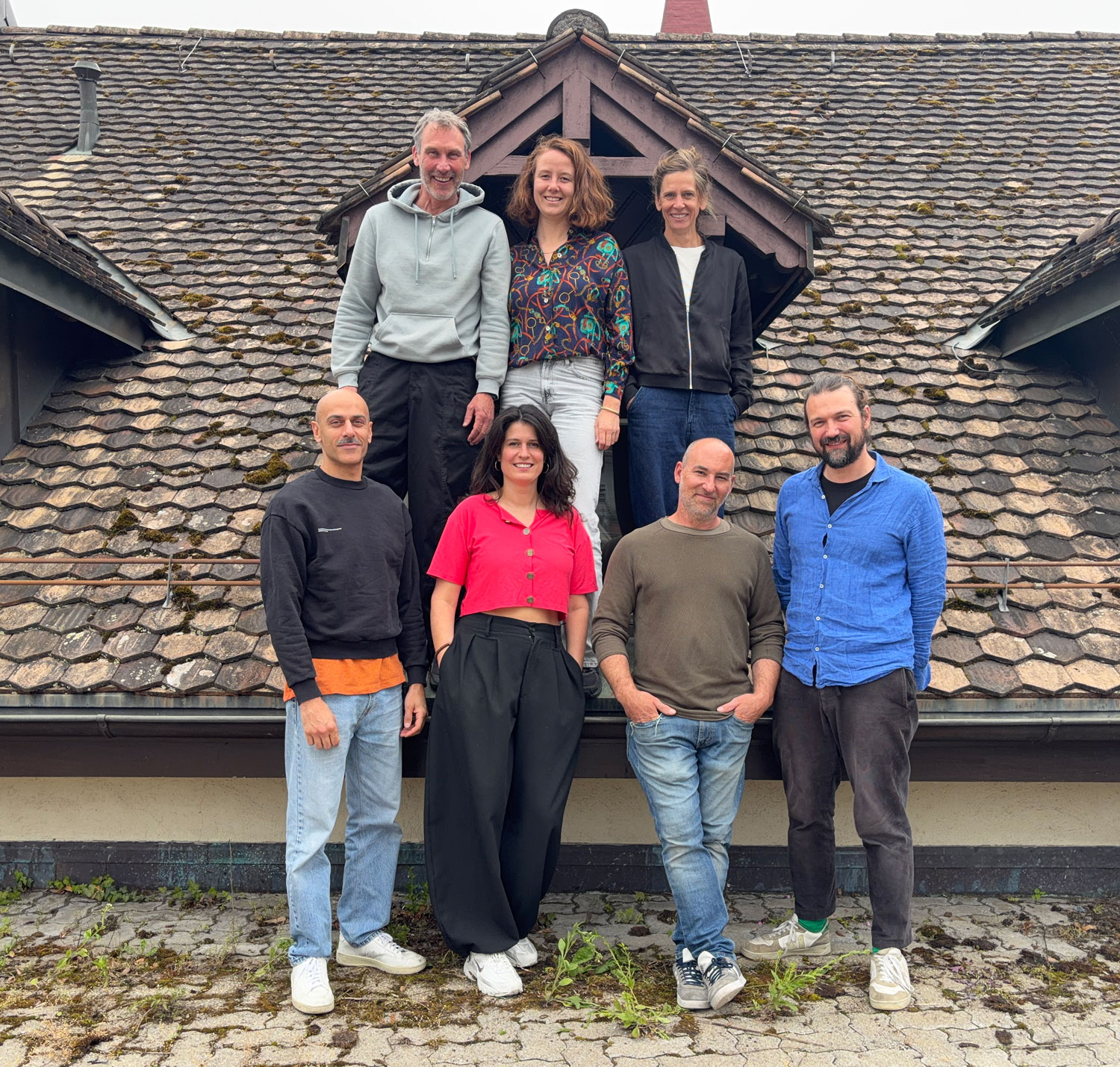 Das Leitungsteam (7 Personen) stehen vor einem Dachfenster und schauen in die Kamera